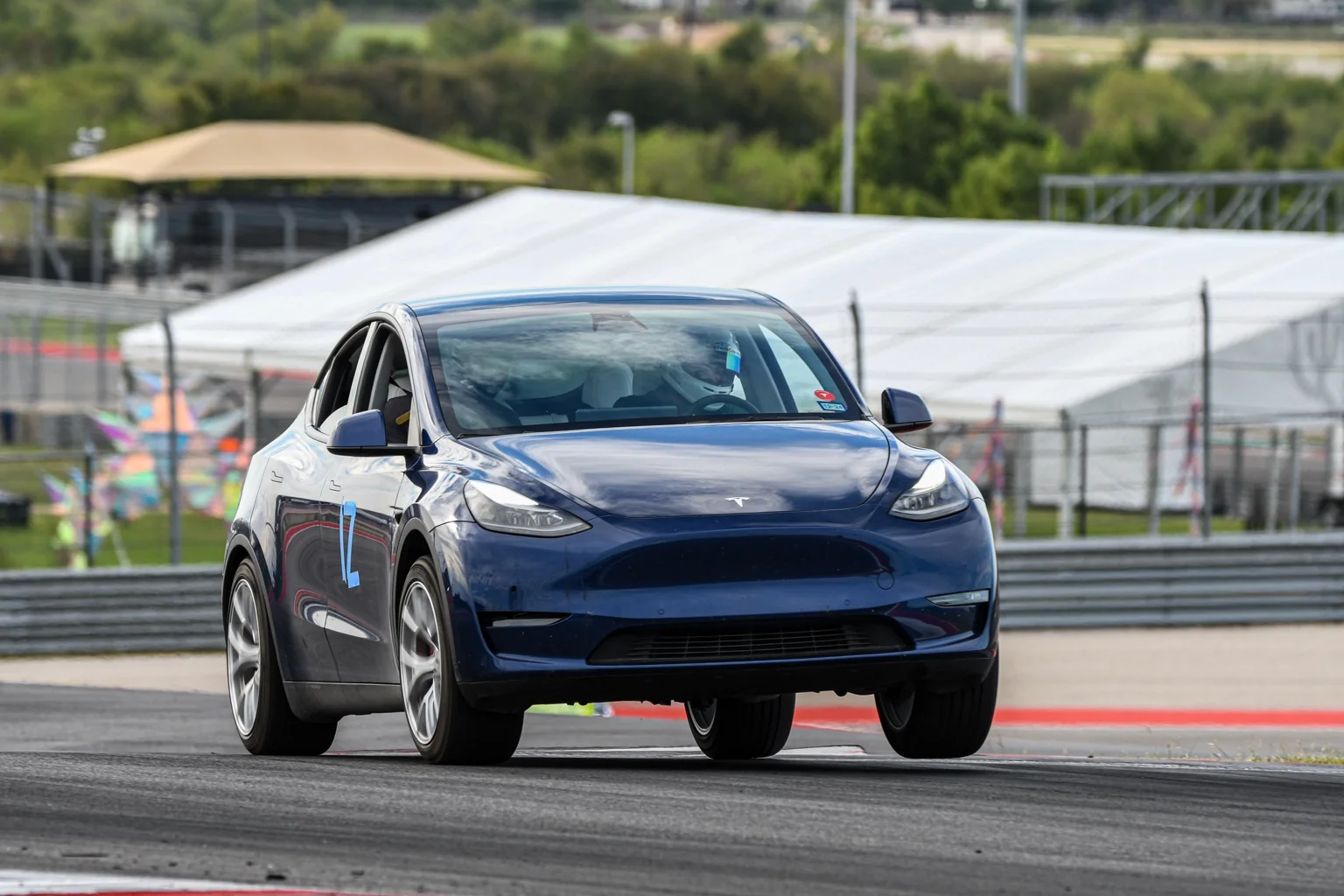 Blue Tesla Model Y cornering at COTA with its inside front wheel lifted off the track