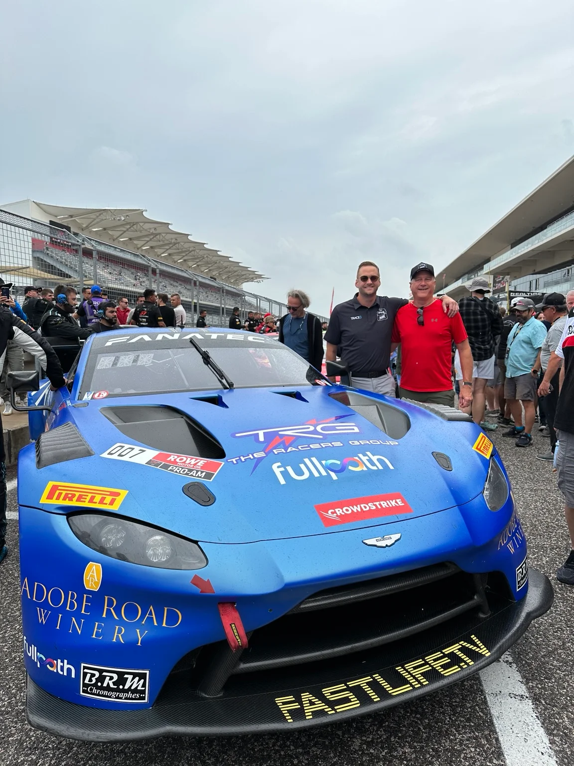 Drew and his dad beside the blue number 007 TRG Aston Martin on the COTA grid